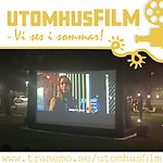 Utomhusskärm med film en mörk kväll. Ljus och bilar parkerade i bakgrunden.