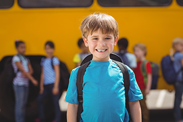 Pojke med ryggsäck framför en skolskjutsbuss