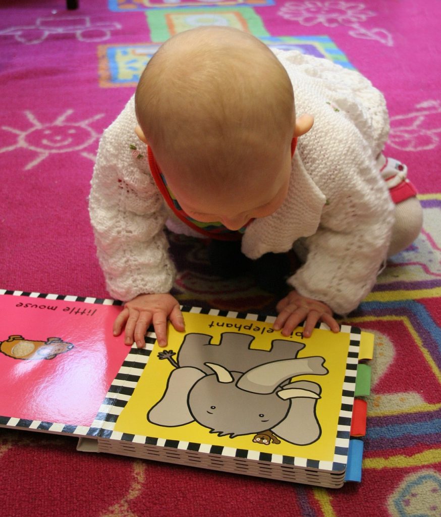 En bebis sitter på golvet och tittar i en bok.