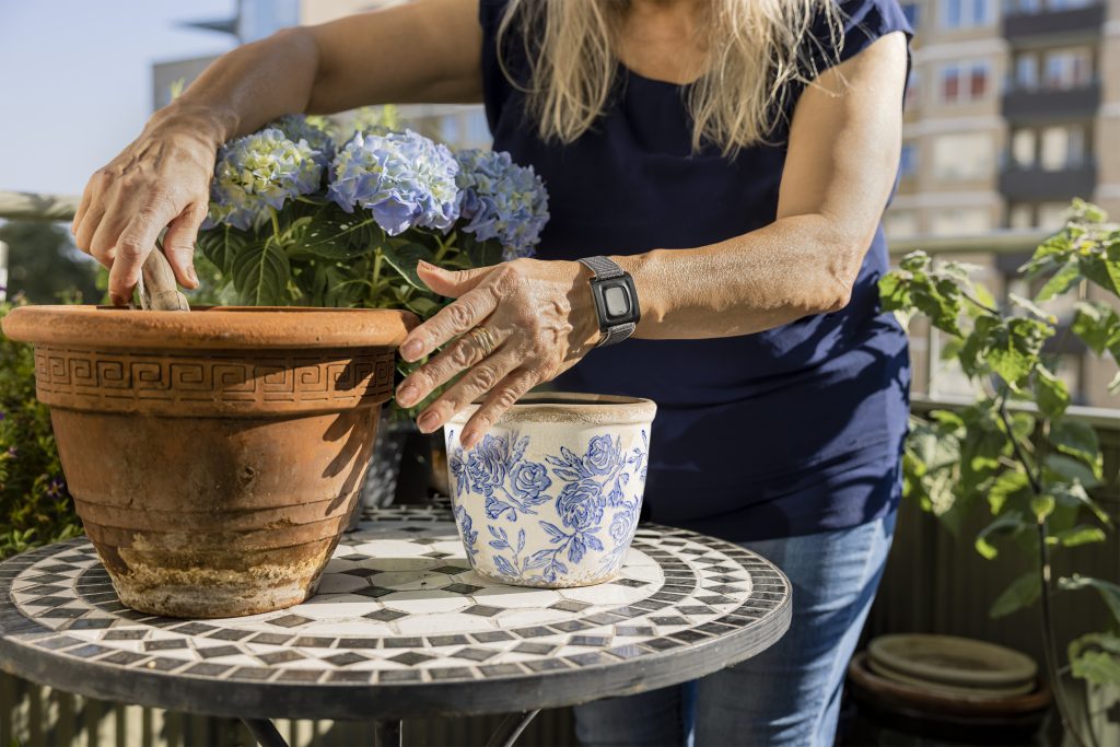Kvinna med trygghetslarm på armen planterar blommor i kruka