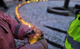 Barnhand med vante håller ljuslykta. Snö och fler ljuslyktor i bakgrunden.