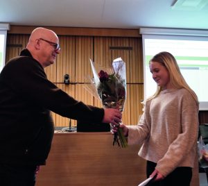 Tjej tar emot blommor av herre i kommunfullmäktigesal